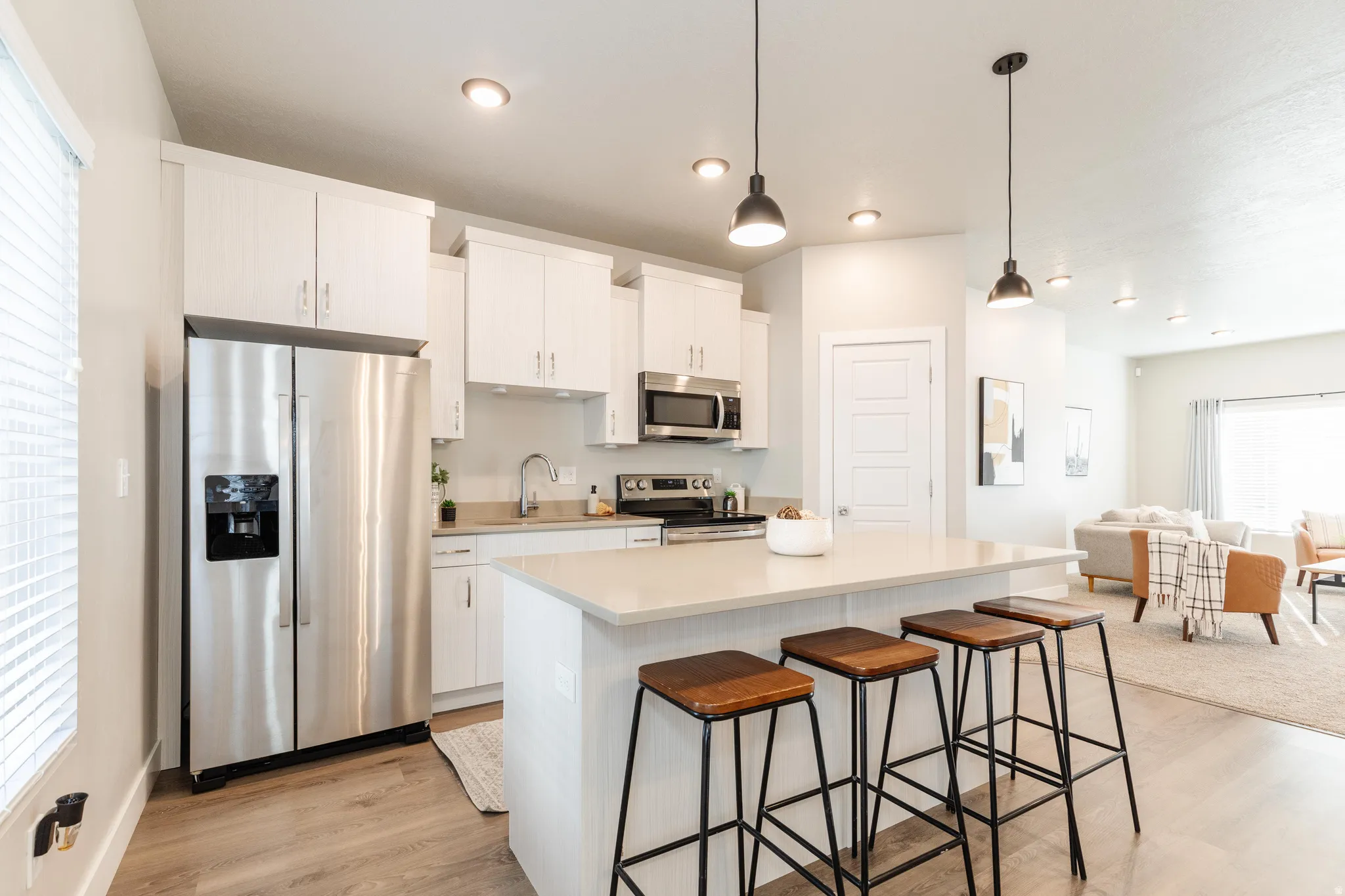 Open-concept kitchen featuring an island with counter seating, stainless steel appliances, white cabinetry, and wood-finish flooring