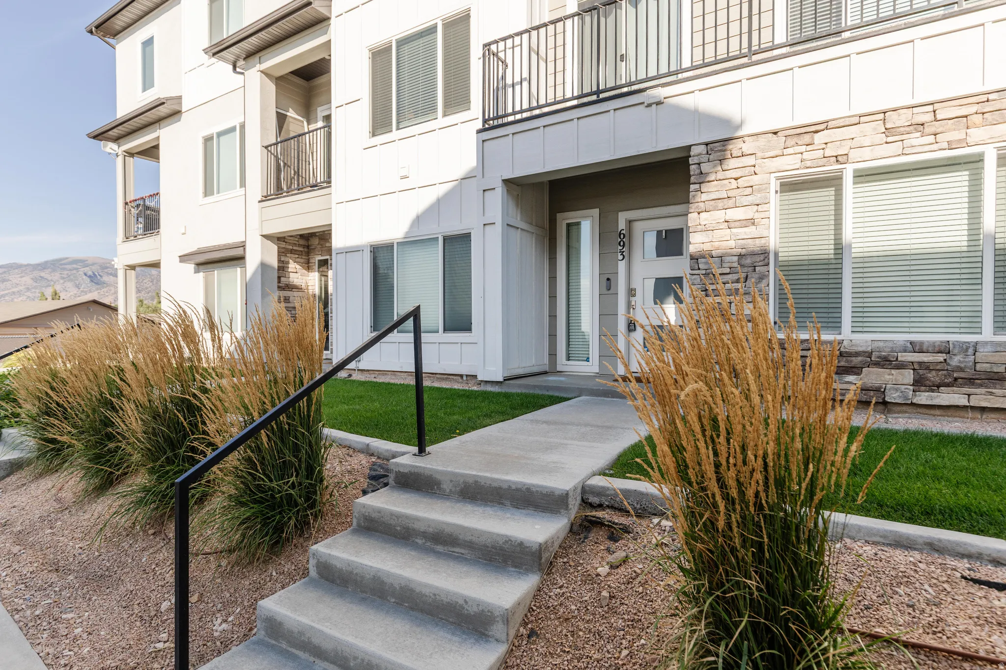 Contemporary multi-story exterior featuring a stone accent facade, a modern entry door with frosted glass panels, and an upper-level balcony with black metal railings