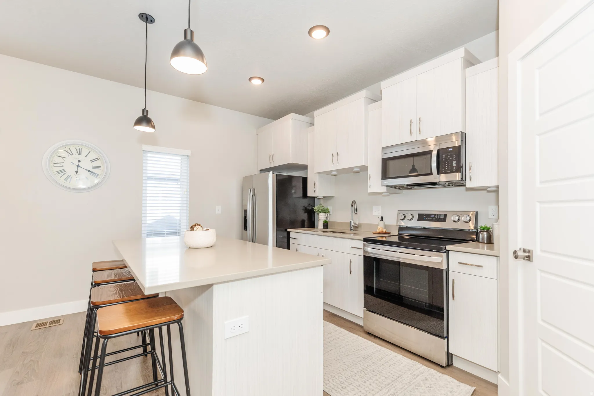 Kitchen featuring an island with seating, pendant lighting, white cabinetry, stainless steel appliances, and wood-finish flooring