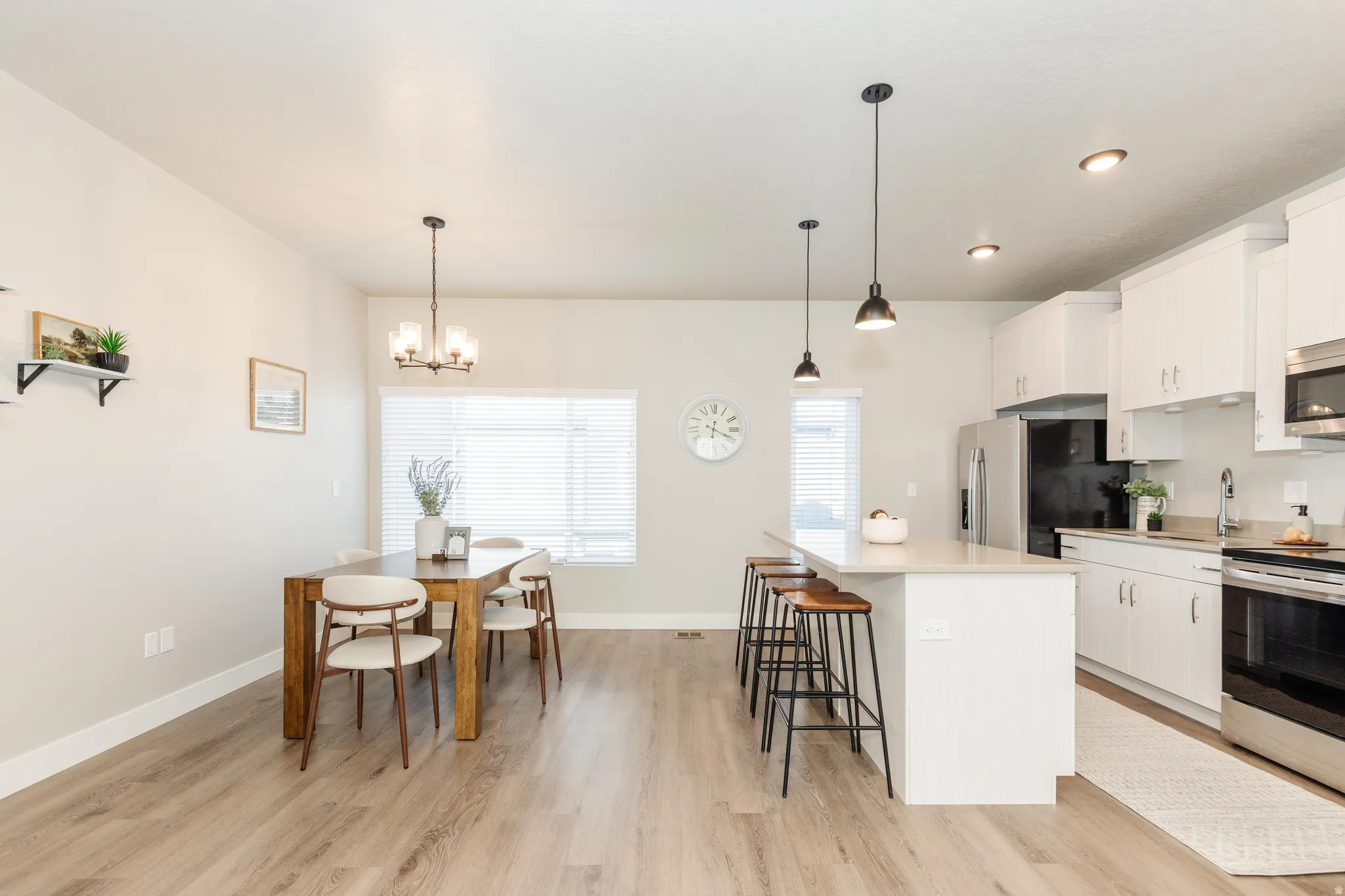 Open-concept kitchen and dining area featuring light-toned wood-finish flooring, white cabinetry, stainless steel appliances, and a central island with countertop seating