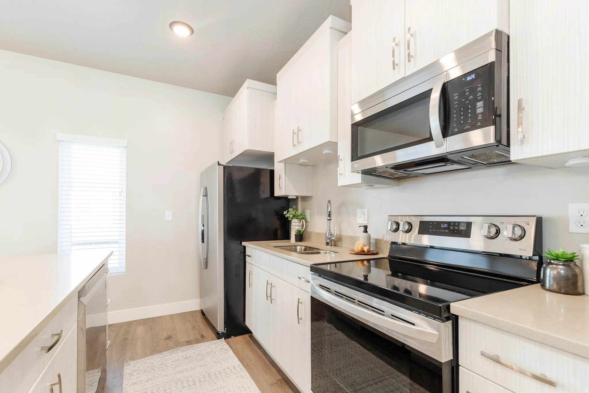 Modern kitchen featuring white cabinetry, stainless steel appliances, wood-finish flooring, recessed lighting, and light-toned countertops