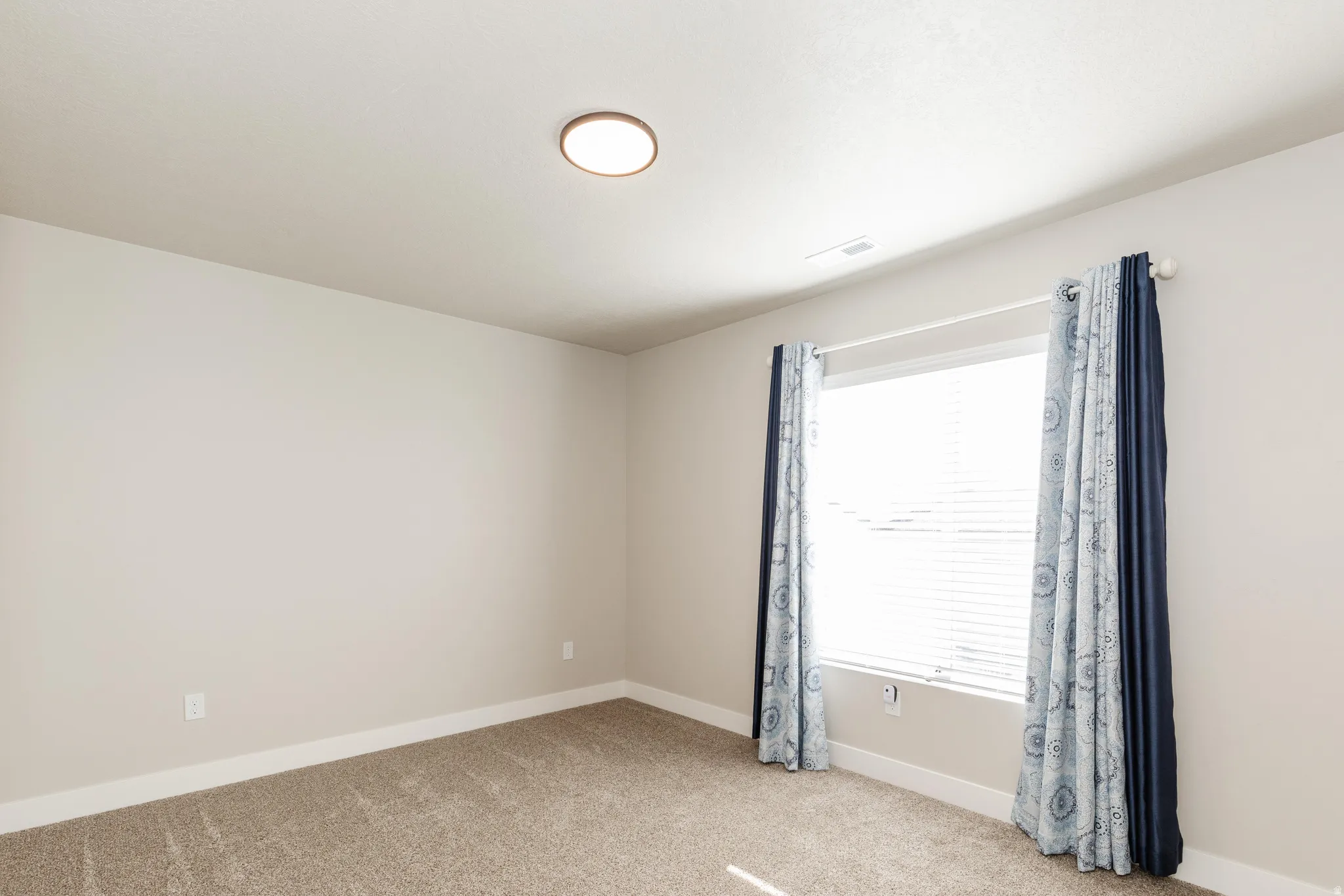 Neutral tone walls featuring a single window with blinds and decorative curtain panels