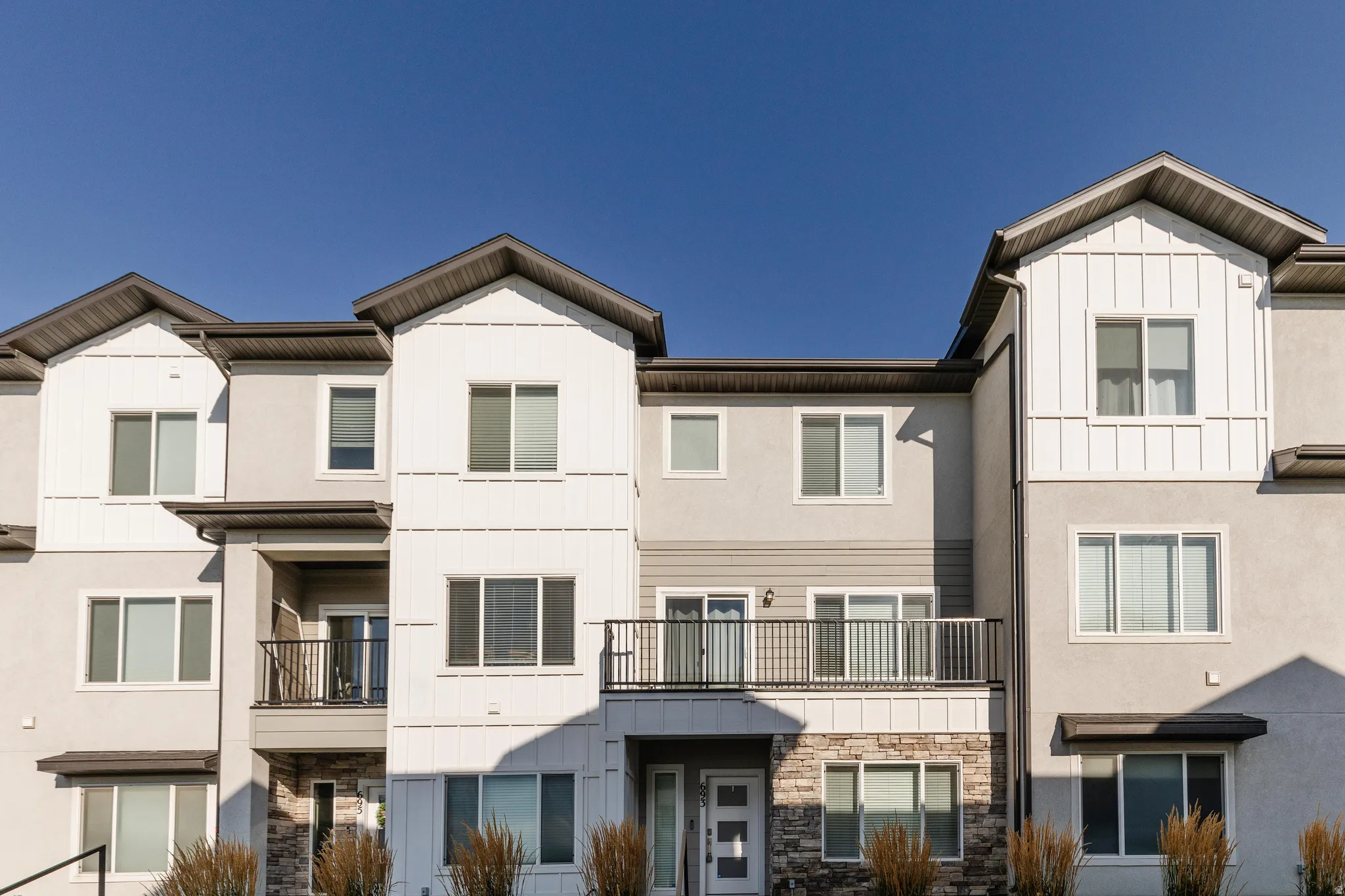 Contemporary multi-level exterior featuring light-toned stucco, contrasting vertical siding accents, black-framed windows, and multiple balconies with dark metal railings