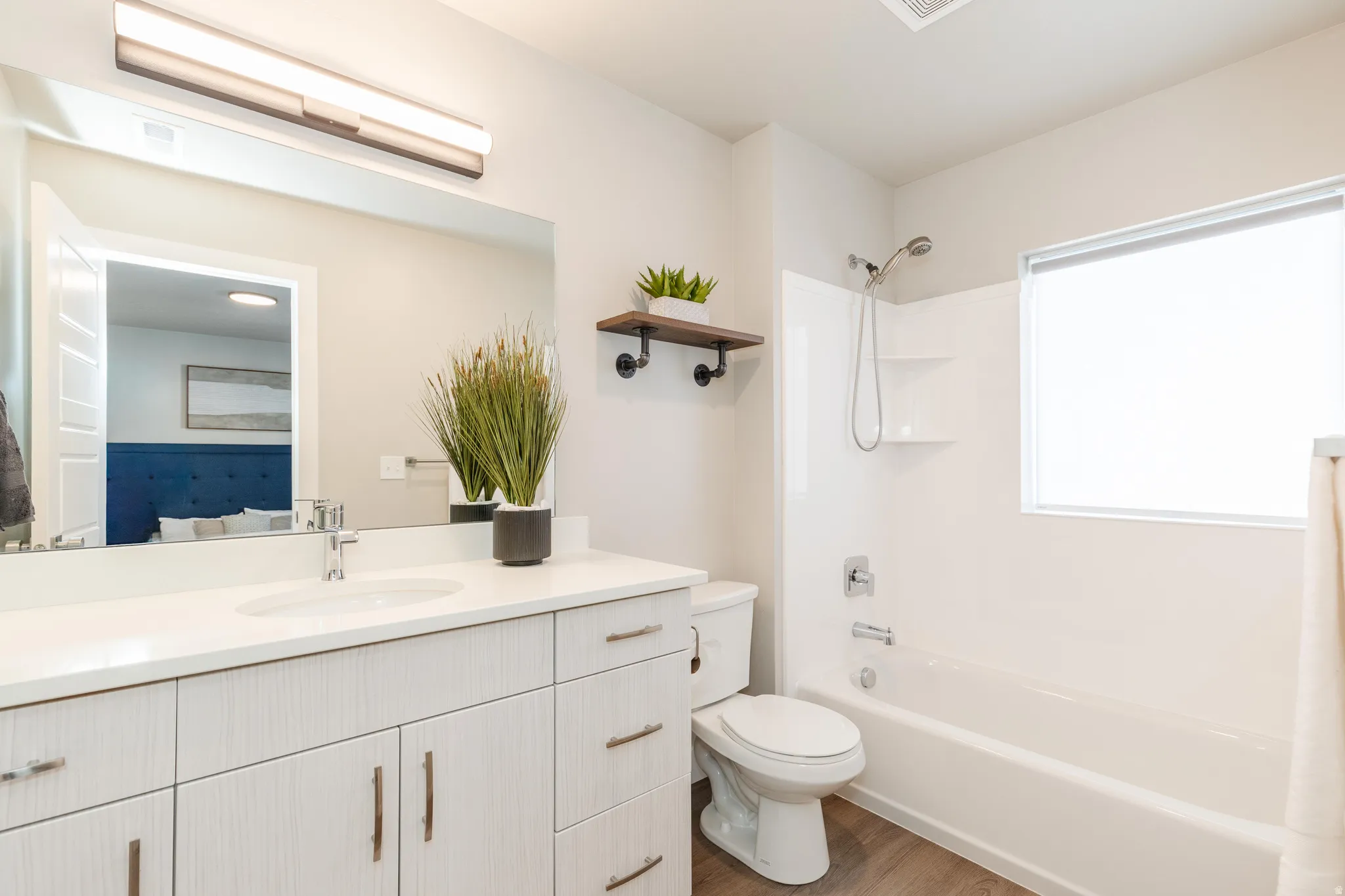 Bathroom featuring a light wood-finish vanity with a white countertop and undermount sink, a large wall mirror, and a white tub/shower combination with chrome fixtures
