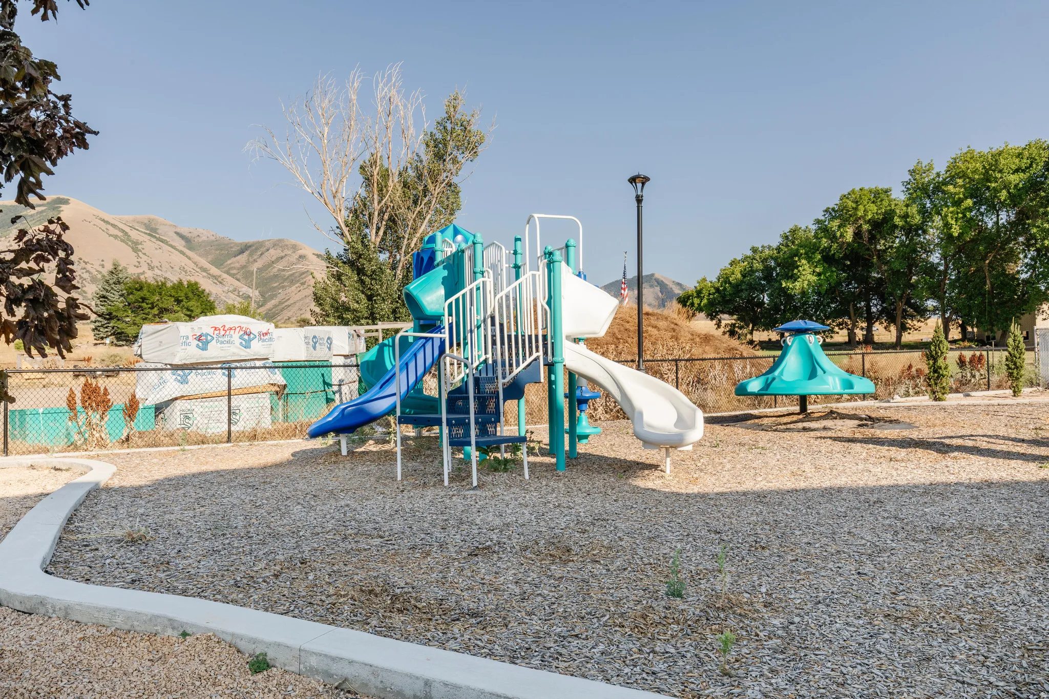 Outdoor play area featuring a multi-level play structure with slides and climbing elements, a separate spinning play feature, and a ground covering of wood chips
