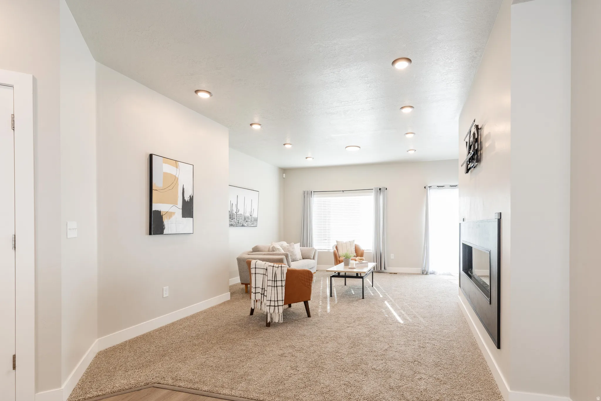 Living area featuring recessed ceiling lighting, a modern horizontal fireplace, light-toned carpeting, a window with vertical blinds, and a glass-paned door