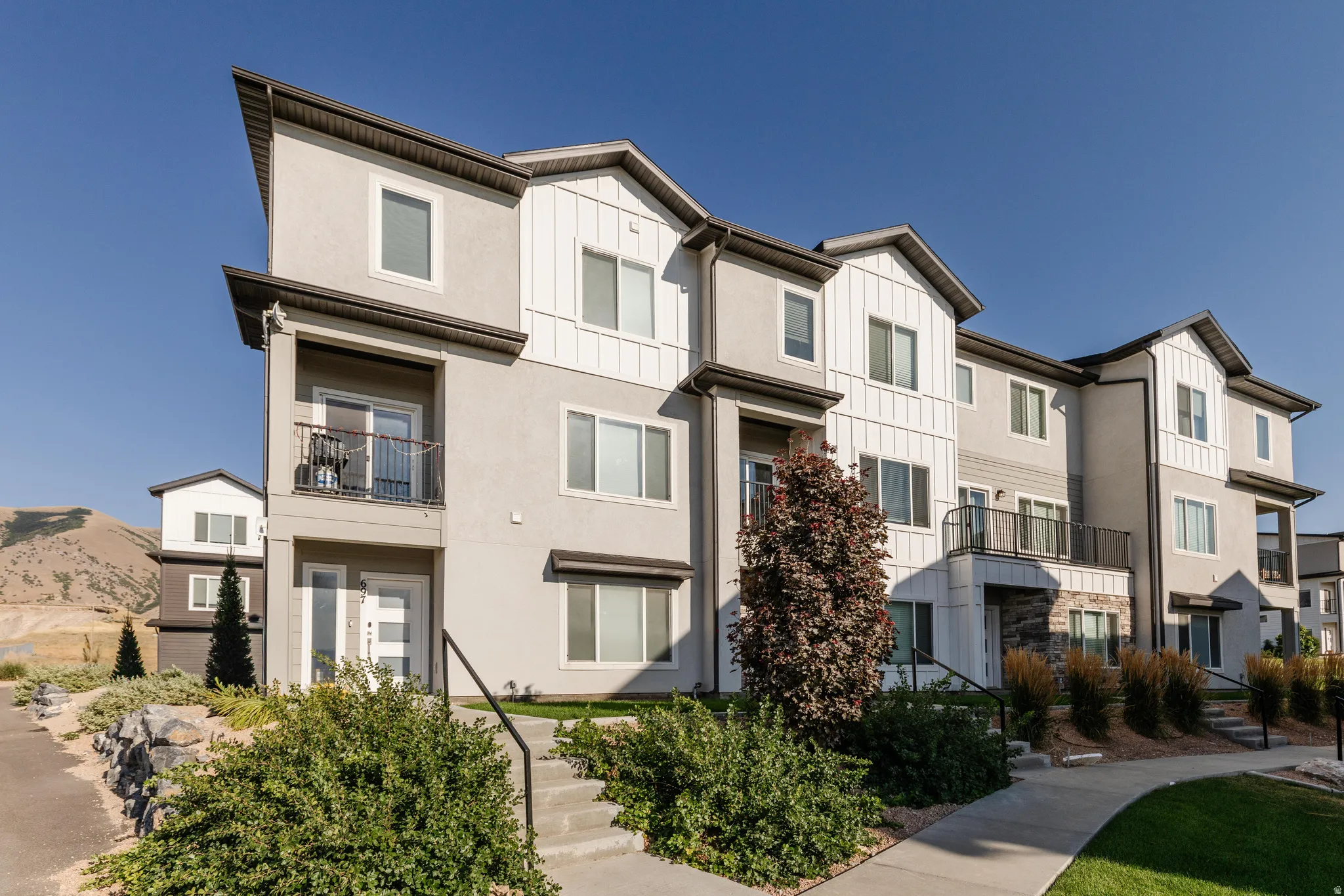 Contemporary multi-story exterior featuring a mix of smooth stucco, vertical white siding, and stone accents