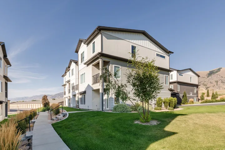 Modern multi-story residential building featuring light-toned siding, dark roofing, and multiple balconies