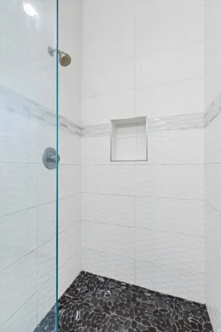 Shower enclosure featuring a frameless glass panel, a rainfall showerhead, and a built-in recessed shelf