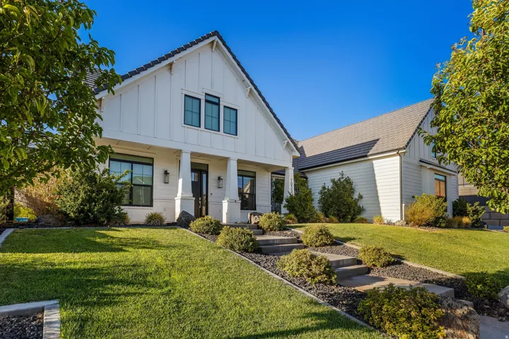 Modern farmhouse exterior with white board and batten siding, dark framed windows, a covered entry with columns, and a dark shingle roof
