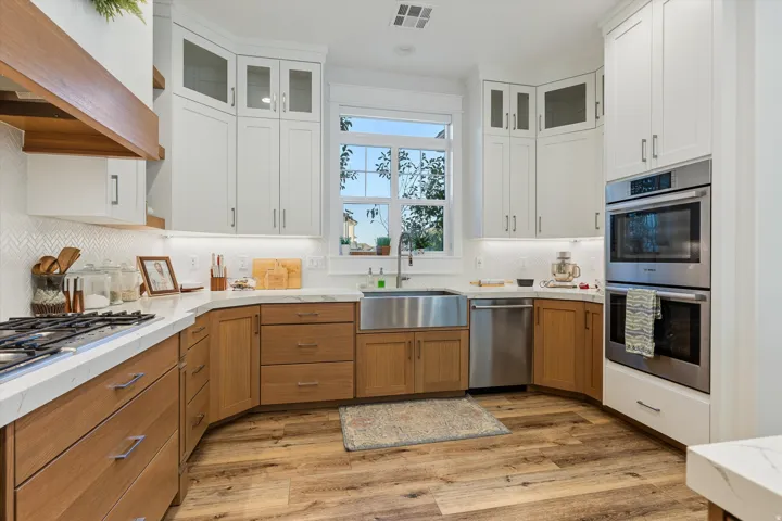 Gourmet kitchen featuring a gas range, built-in double ovens, farmhouse sink, quartz countertops, and wood-finish flooring