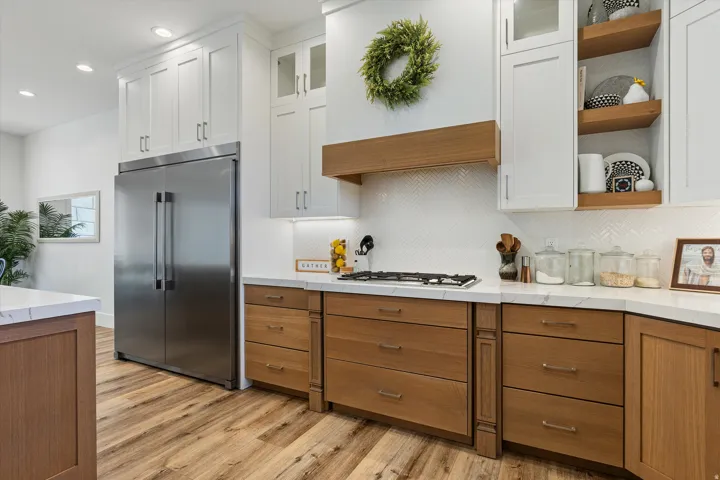 Gourmet kitchen featuring a stainless steel refrigerator, gas cooktop, wood-finish flooring, white shaker cabinetry, and wood-toned lower cabinetry with white countertops