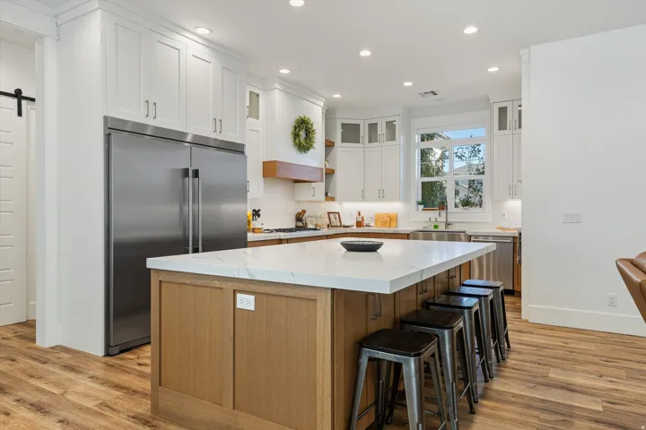 Gourmet kitchen featuring a substantial central island with seating, stainless steel appliances, white shaker cabinetry, and wood-finish flooring