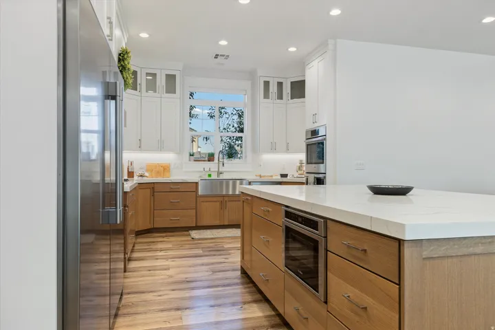 Gourmet kitchen featuring a large central island with integrated microwave, stainless steel appliances, wood-finish flooring, two-tone cabinetry, and recessed lighting