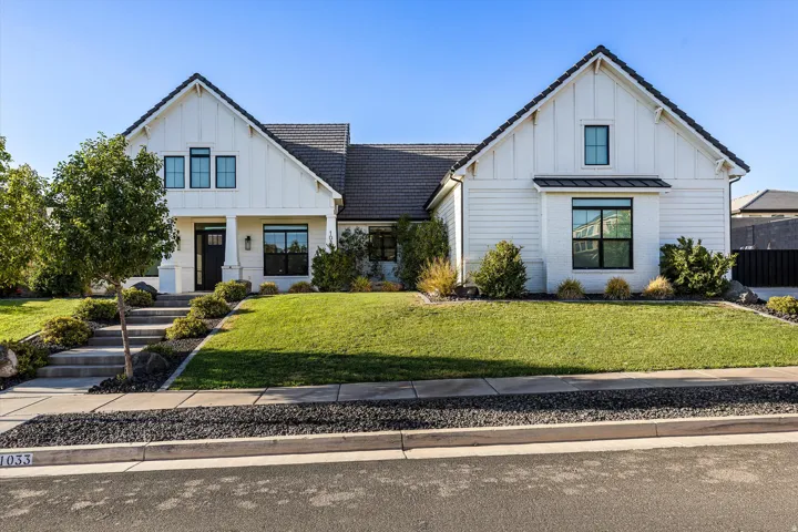 Modern farmhouse exterior featuring white board and batten siding, dark framed windows, a covered entry with a dark door, and a manicured front lawn