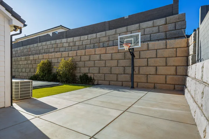 Paved concrete patio area with a built-in basketball hoop, artificial turf section, and decorative retaining walls