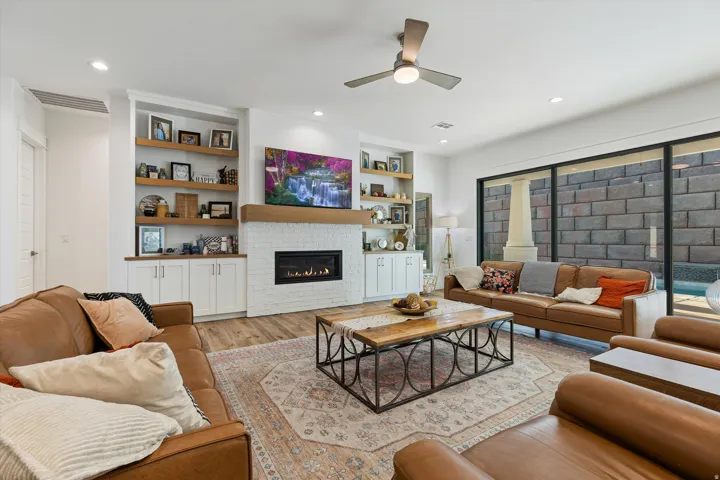 Spacious living area featuring wood-finish flooring, a contemporary fireplace with a white brick surround, and built-in shelving with integrated cabinetry