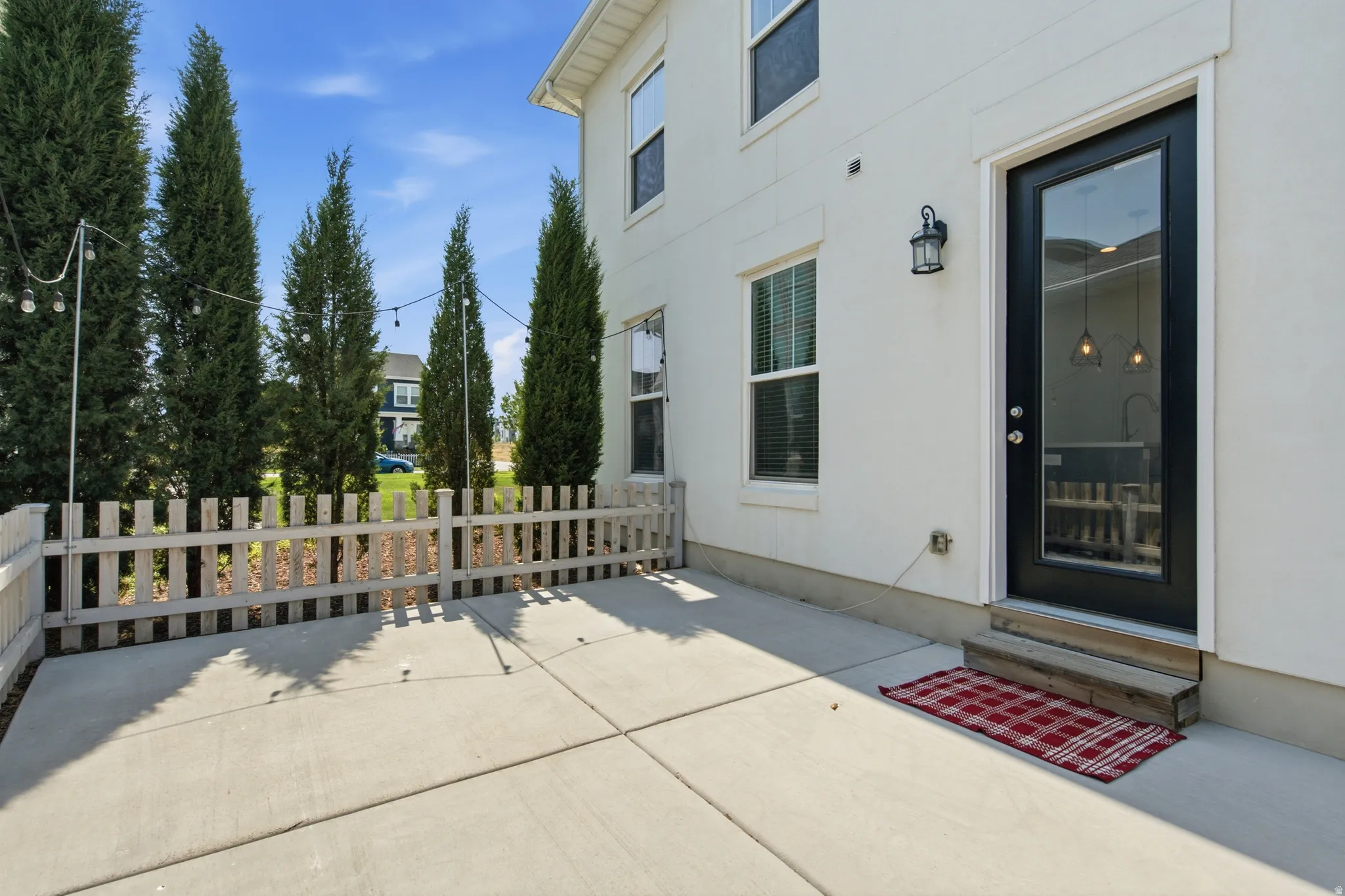 Concrete patio with a white picket fence and privacy landscaping