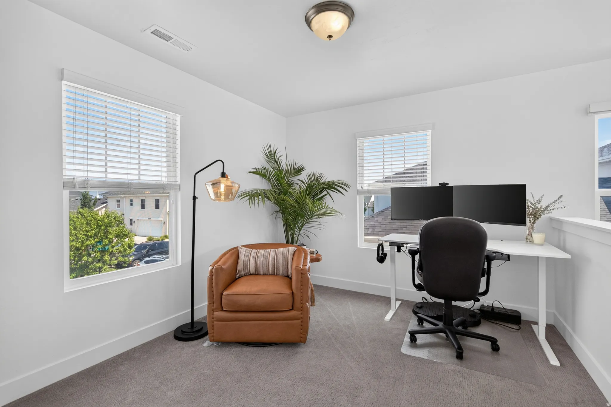 Bright room featuring multiple windows with blinds, light gray carpet flooring, and a white railing