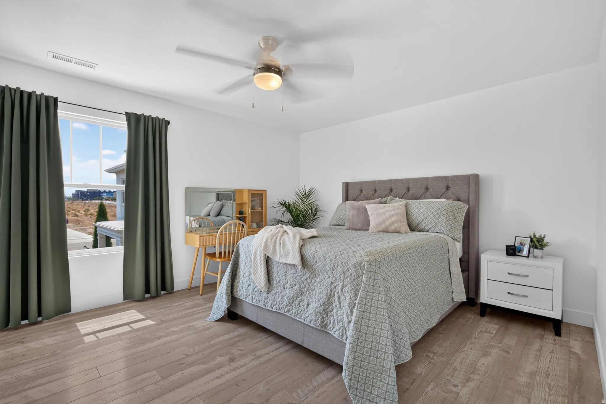Bright bedroom featuring light wood-finish flooring, white walls, and a window with dark curtains