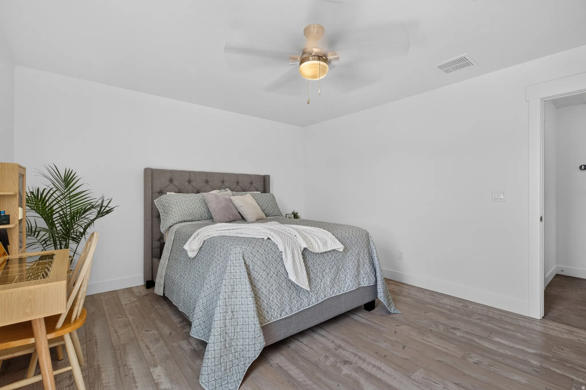 Light-toned wood-finish flooring complements the white walls of this bedroom, featuring a tufted fabric headboard
