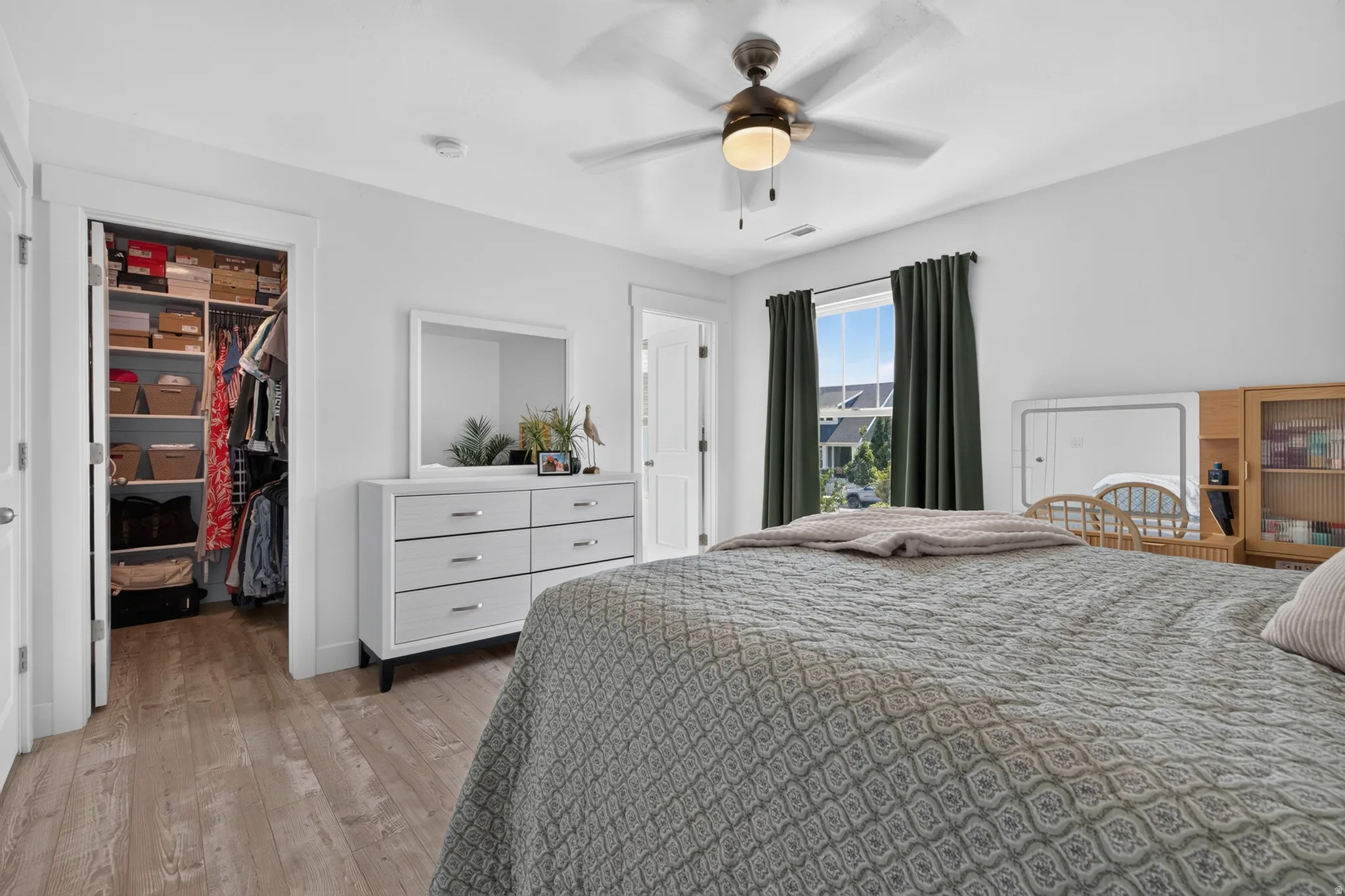 Bedroom featuring wood-finish flooring, a ceiling fan with integrated lighting, and a window with dark curtain rods