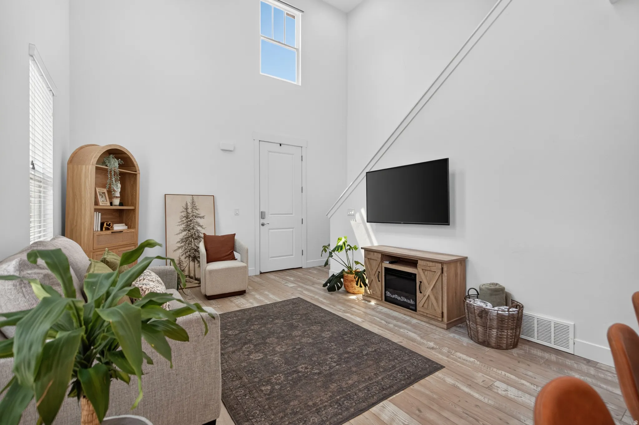 Two-story living area featuring wood-finish flooring, a contemporary accent wall, and a high window