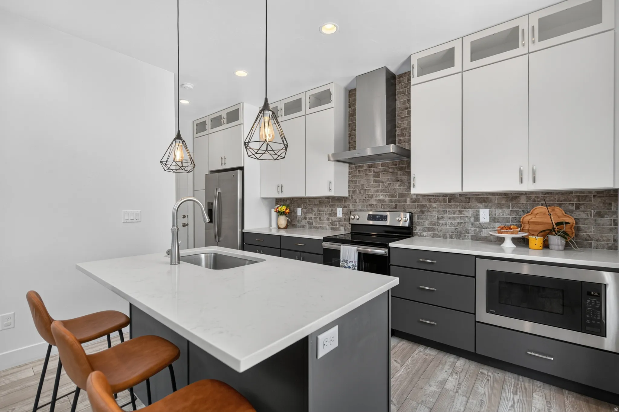 Contemporary kitchen featuring a two-tone cabinetry design with white upper cabinets and charcoal lower cabinetry, quartz waterfall-edge island countertop, stainless steel appliances including a built-in wall oven, subway tile backsplash, pendant lighting