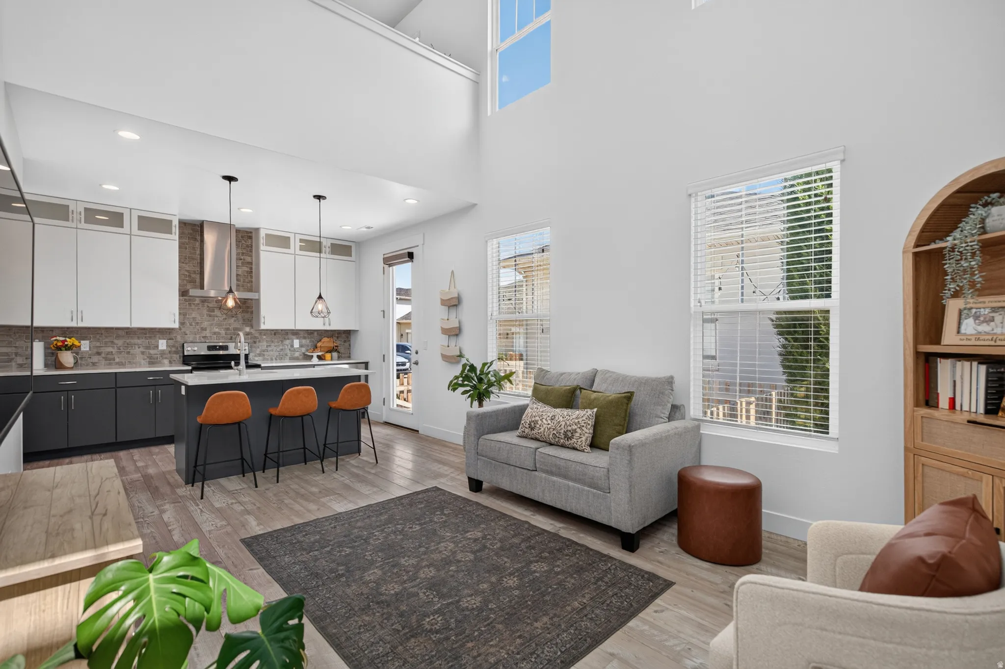 Open-concept living space featuring a two-story ceiling, wood-finish flooring, a kitchen island with pendant lighting, a tile backsplash, and stainless steel appliances