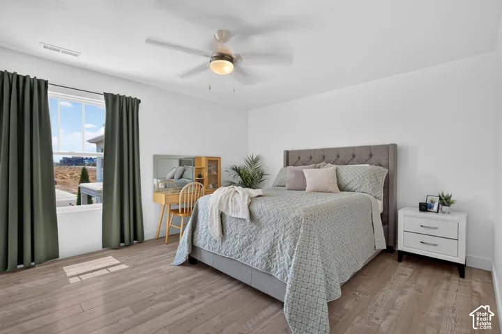 Bright bedroom featuring light wood-finish flooring, white walls, and a window with dark curtains