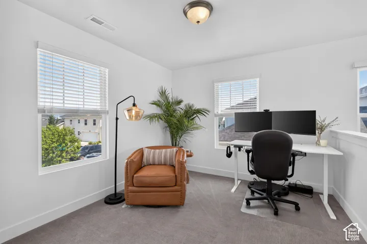 Bright room featuring multiple windows with blinds, light gray carpet flooring, and a white railing