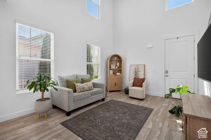 Living area featuring high ceilings, upper transom windows, two large windows with blinds, light wood-finish flooring, and a modern white door with brushed nickel hardware