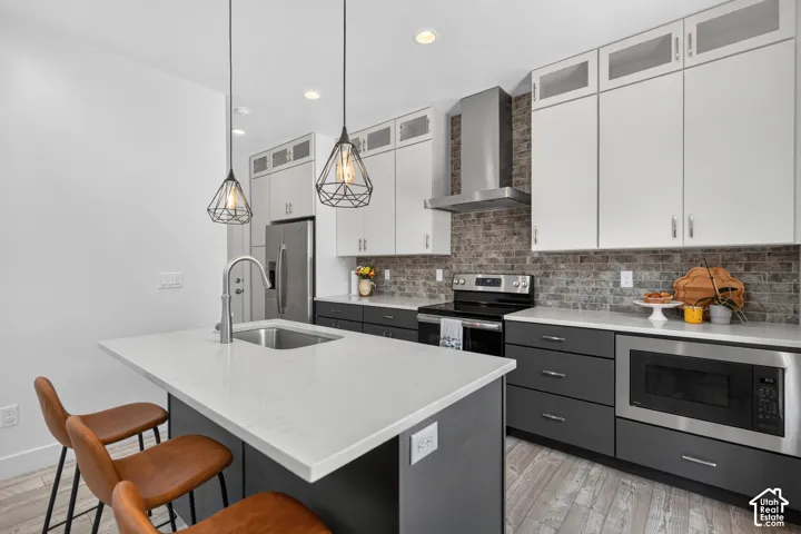 Contemporary kitchen featuring a two-tone cabinetry design with white upper cabinets and charcoal lower cabinetry, quartz waterfall-edge island countertop, stainless steel appliances including a built-in wall oven, subway tile backsplash, pendant lighting