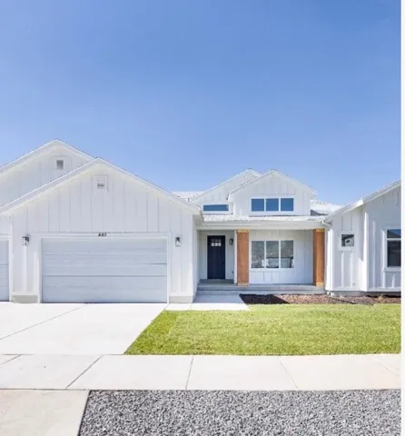 Modern farmhouse exterior featuring white board and batten siding, a dark entry door with clear glass panels, a front porch with natural wood columns, a two-car garage, and a manicured lawn