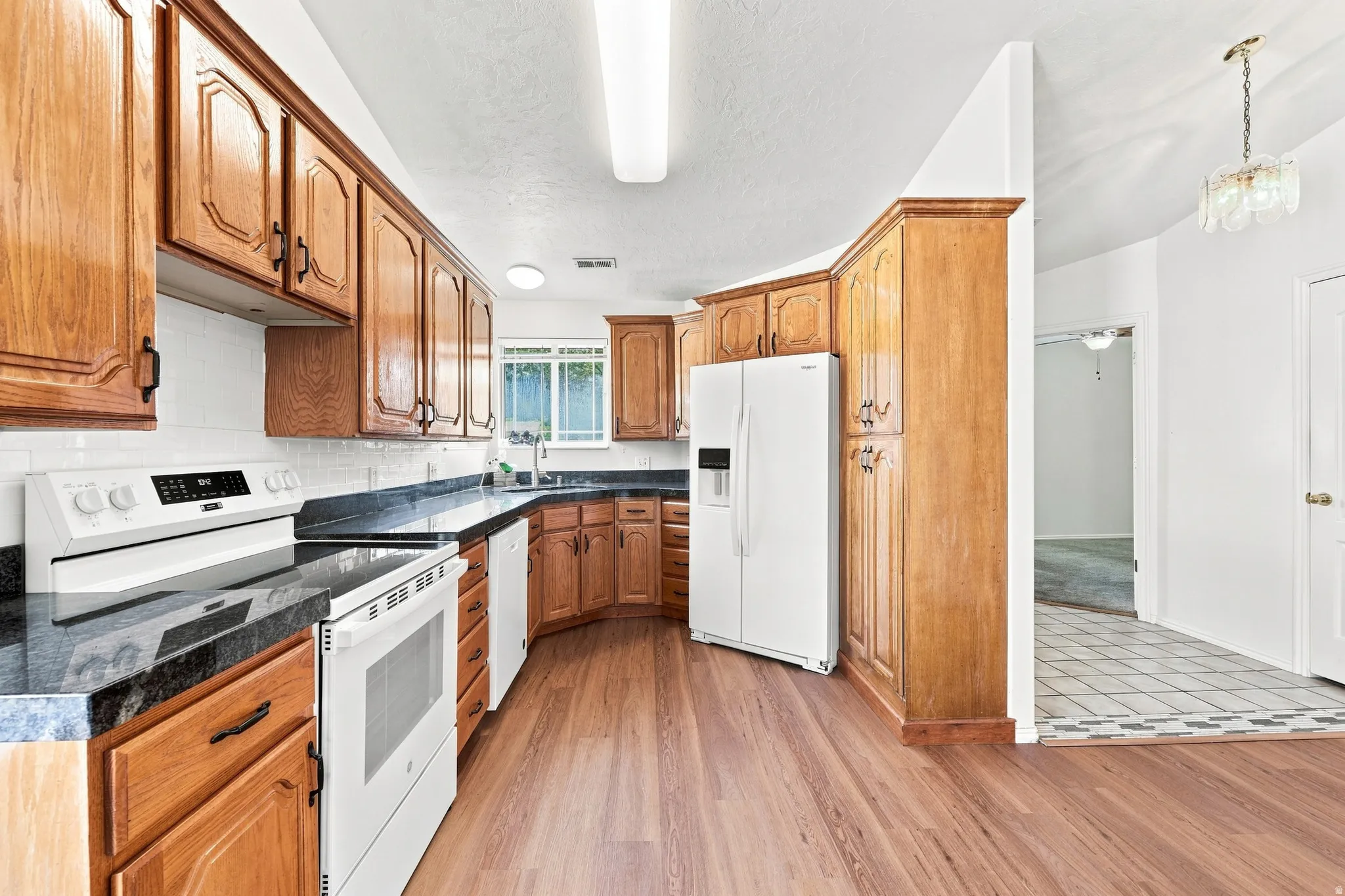 Kitchen featuring wood cabinetry, dark countertops, white tile backsplash, and wood-finish flooring