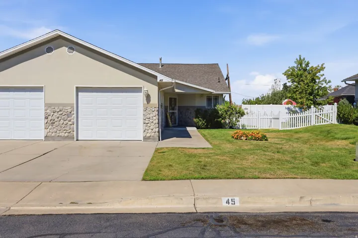 Exterior featuring a two-car garage with panel doors, stone veneer accents, and a stucco finish