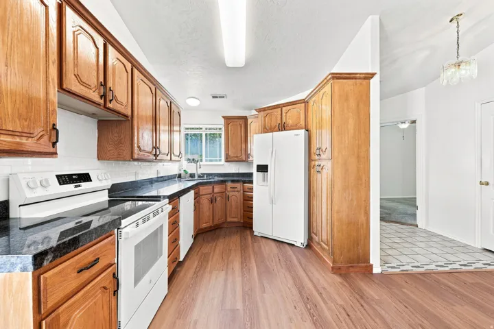 Kitchen featuring wood cabinetry, dark countertops, white tile backsplash, and wood-finish flooring