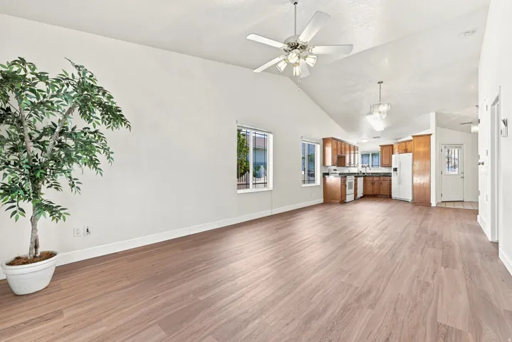 Spacious open-concept living area featuring vaulted ceilings, wood-finish flooring, and multiple windows