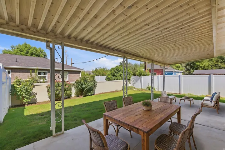 Expansive covered patio featuring a slatted wood-finish ceiling, concrete flooring, decorative metal support columns, and privacy fencing
