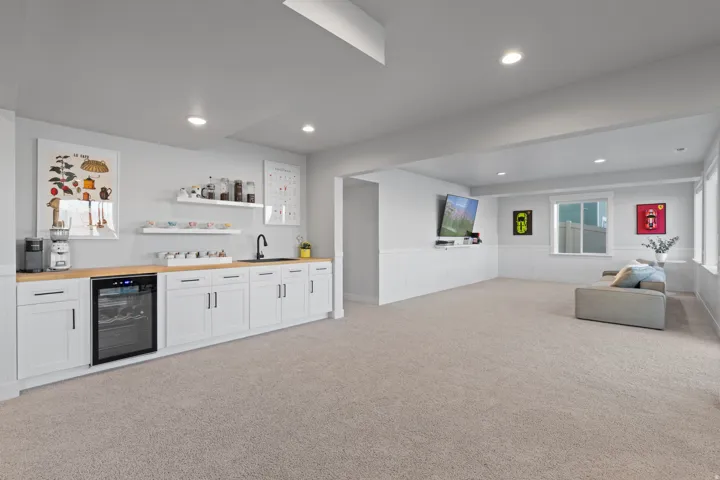Spacious recreational room featuring a wet bar with white cabinetry, light wood-finish countertops, an undermount sink, and a built-in beverage refrigerator