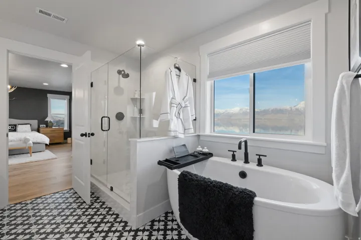 Freestanding soaking tub with matte black fixtures, set against a window with mountain and water scenery