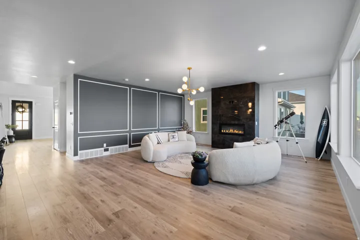 Spacious living area featuring wood-finish flooring, a contemporary fireplace with a dark stone surround, and multiple large windows