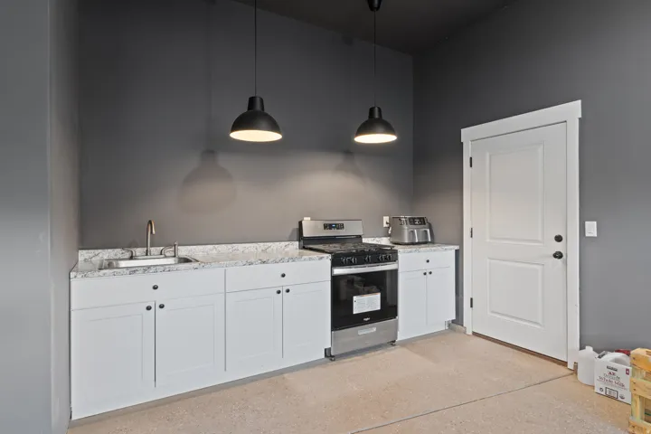 Kitchenette featuring white cabinetry, light-colored countertops, a stainless steel gas range, a stainless steel sink with a brass faucet, and two industrial-style pendant lights