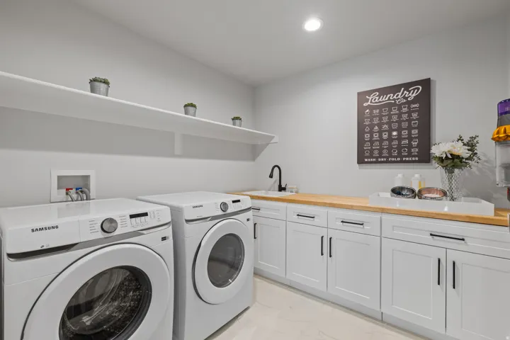 Dedicated utility space featuring open shelving, a built-in sink with a matte black faucet, wood-finish countertops, and white cabinetry with black hardware