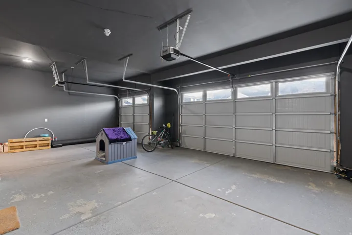 Spacious two-car garage featuring a concrete floor, dark gray painted walls, and overhead lighting