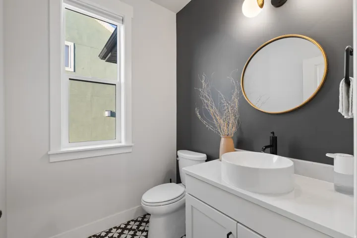 Powder room featuring a white single-sink vanity with a quartz countertop, an oval vessel sink, and matte black fixtures