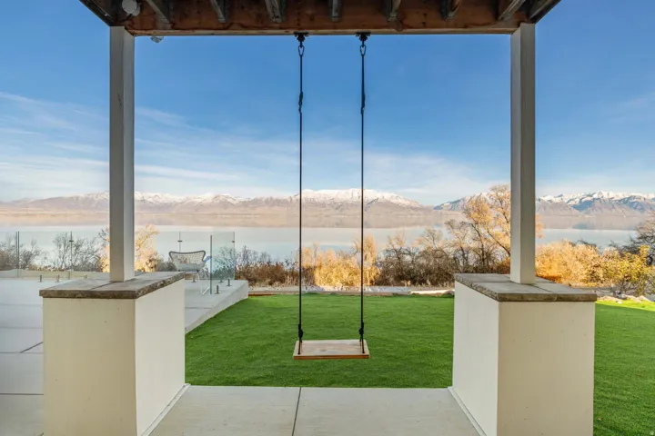 Covered patio area with a concrete surface, featuring a suspended wooden swing and robust support columns