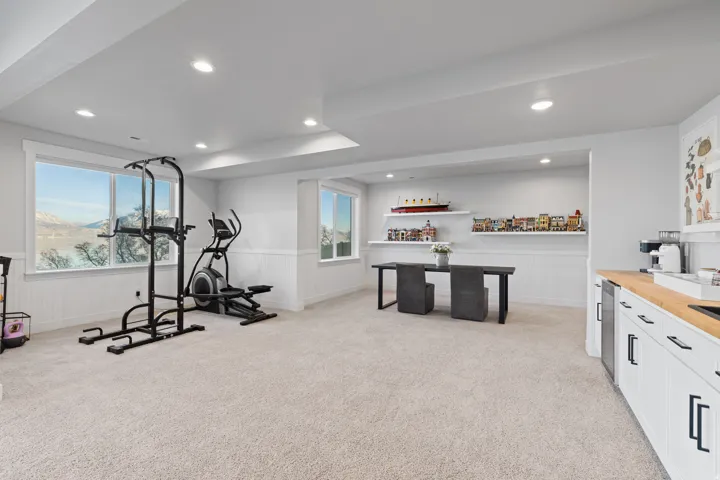 Spacious finished basement featuring recessed lighting, large windows, light-toned carpet flooring, a built-in wet bar with a wood-finish countertop, and integrated shelving