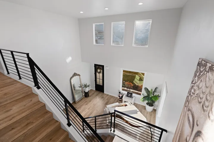 Two-story entryway featuring wood-finish flooring, a contemporary black metal staircase railing, recessed lighting, and high windows providing natural light