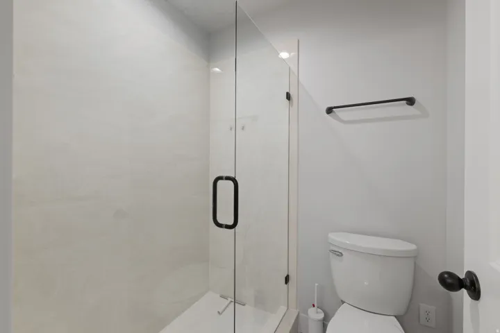 Enclosed shower with clear glass door and black hardware, complemented by a white toilet and a black towel bar